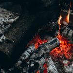 A detailed view of glowing embers and burnt wood with rising smoke.