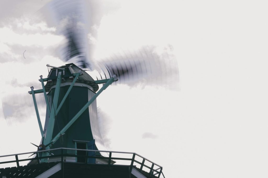 Windmill in motion with blurred blades set against a backdrop of a cloudy sky, symbolizing renewable energy.