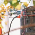 Close-up of an electric car connected to a charging station outdoors in sunlight.