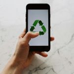 Hand holding smartphone displaying recycling symbol, promoting eco-friendly technology.