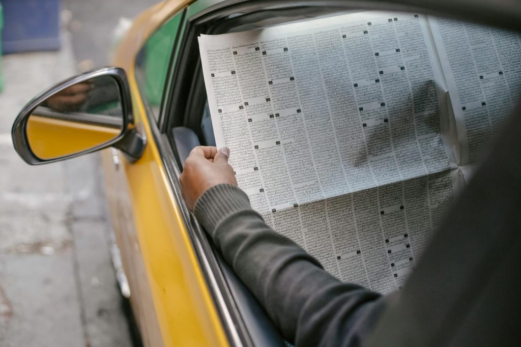 A person reads a newspaper through a car window, capturing a moment of leisure and information.