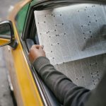 A person reads a newspaper through a car window, capturing a moment of leisure and information.