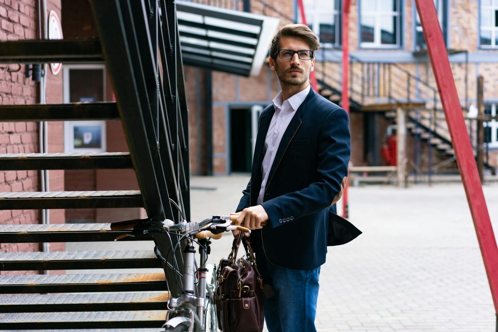 Elegant businessman with bicycle in cityscape, wearing a suit and carrying a briefcase.