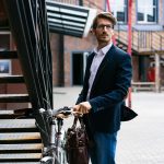 Elegant businessman with bicycle in cityscape, wearing a suit and carrying a briefcase.