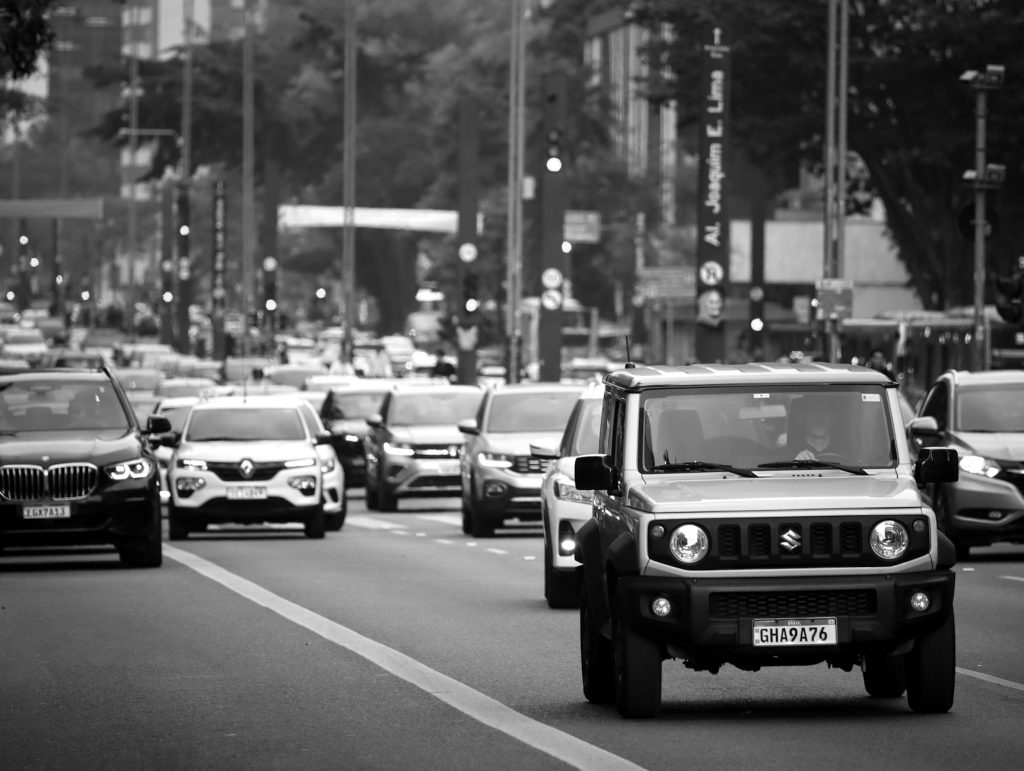 A busy city street scene with various cars in motion, captured in black and white.