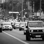 A busy city street scene with various cars in motion, captured in black and white.