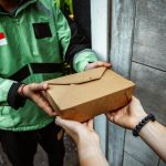 A delivery person hands over a cardboard lunchbox to a customer, showcasing food delivery service.