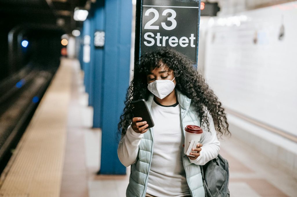 African American woman using phone at 23 Street subway, NYC. COVID-19 precautions.
