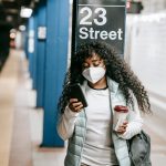 African American woman using phone at 23 Street subway, NYC. COVID-19 precautions.