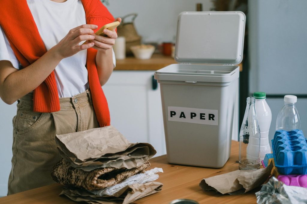 A person sorting recyclable materials into a labeled paper bin in a kitchen setting.