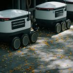 Futuristic delivery robots navigating a leaf-strewn sidewalk, showcasing innovation in modern urban logistics.