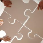 Low angle view of diverse team assembling large puzzle pieces, symbolizing unity and cooperation.