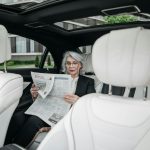 Elderly woman in car reading a newspaper, showcasing a moment of relaxation and focus.