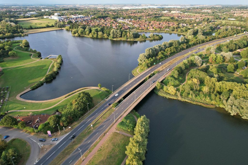 Aerial view of a bridge over a scenic lake surrounded by lush greenery in Caldecotte, England.