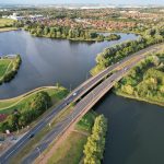 Aerial view of a bridge over a scenic lake surrounded by lush greenery in Caldecotte, England.