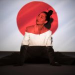 Asian woman poses with Japanese flag projection, embodying cultural symbolism.