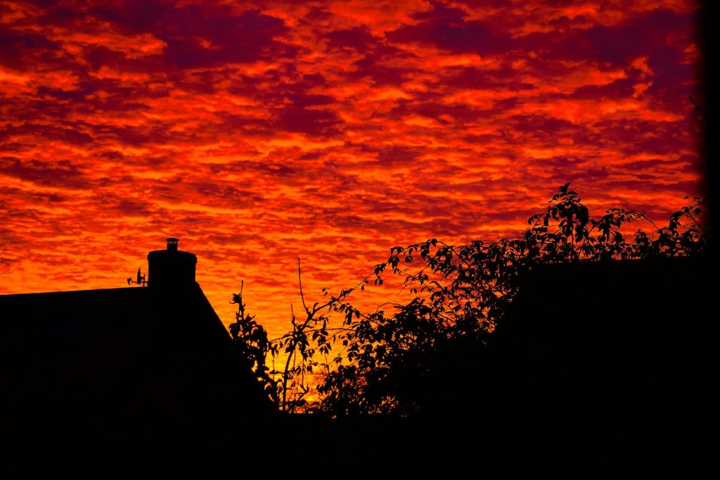 Silhouetted rooftops and foliage against a vivid sunset sky in Milton Keynes.