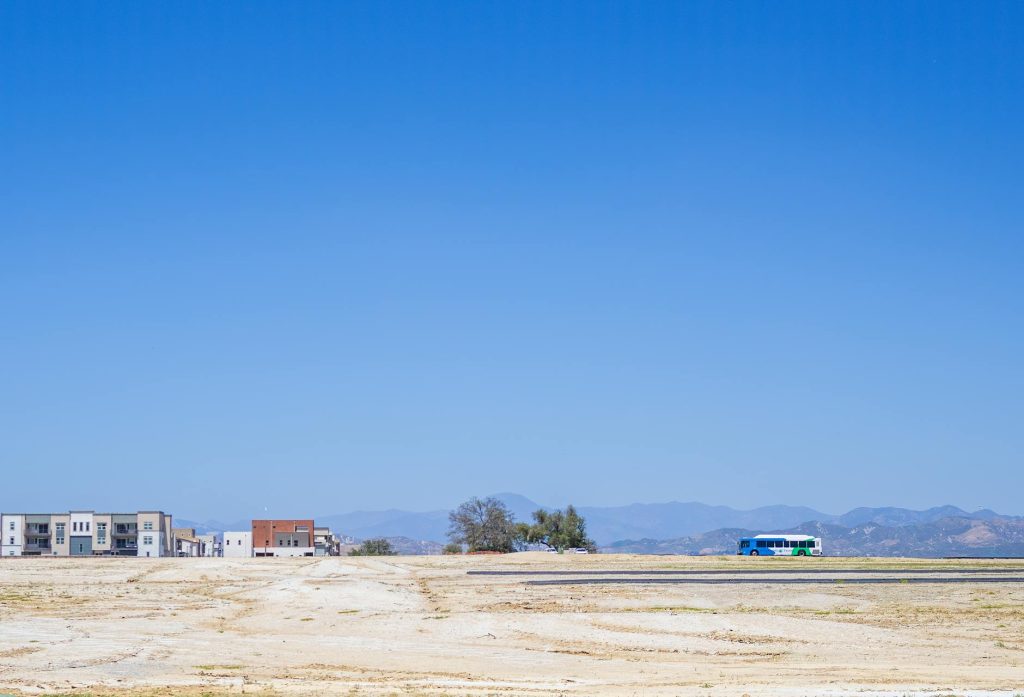 A quiet urban landscape featuring a barren land and a distant bus under a clear blue sky.