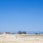 A quiet urban landscape featuring a barren land and a distant bus under a clear blue sky.