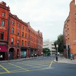A bustling urban street with red brick buildings and a green bus passing by.