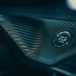 Detailed view of a car's engine start button set in sleek carbon fiber interior.