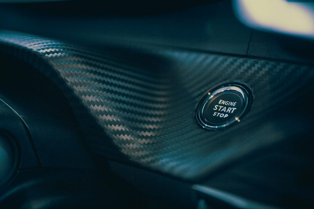 Detailed view of a car's engine start button set in sleek carbon fiber interior.