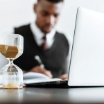 Businessman at desk with hourglass indicating time management and daily work routine.