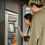 Young couple smiles while purchasing tickets at a station vending machine.