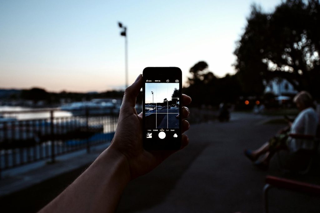 A hand holding a smartphone captures a serene evening park scene.