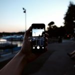 A hand holding a smartphone captures a serene evening park scene.