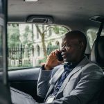 African American businessman in a suit having a phone conversation while traveling in a car in an urban setting.