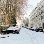 A tranquil snowy street with parked cars and historical architecture in London.