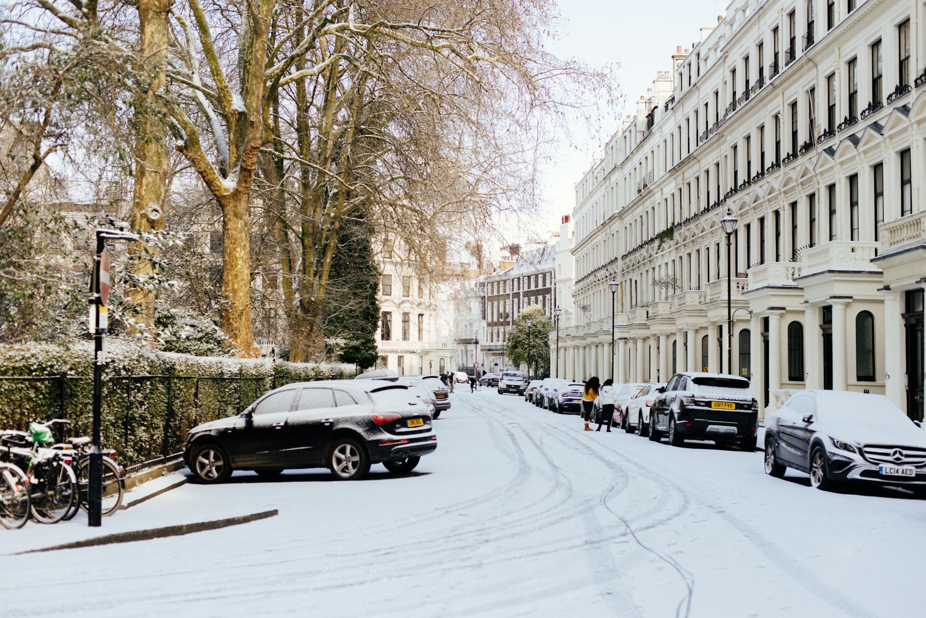 A tranquil snowy street with parked cars and historical architecture in London.