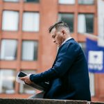 Businessman reviews documents outside with a tablet in a city setting.