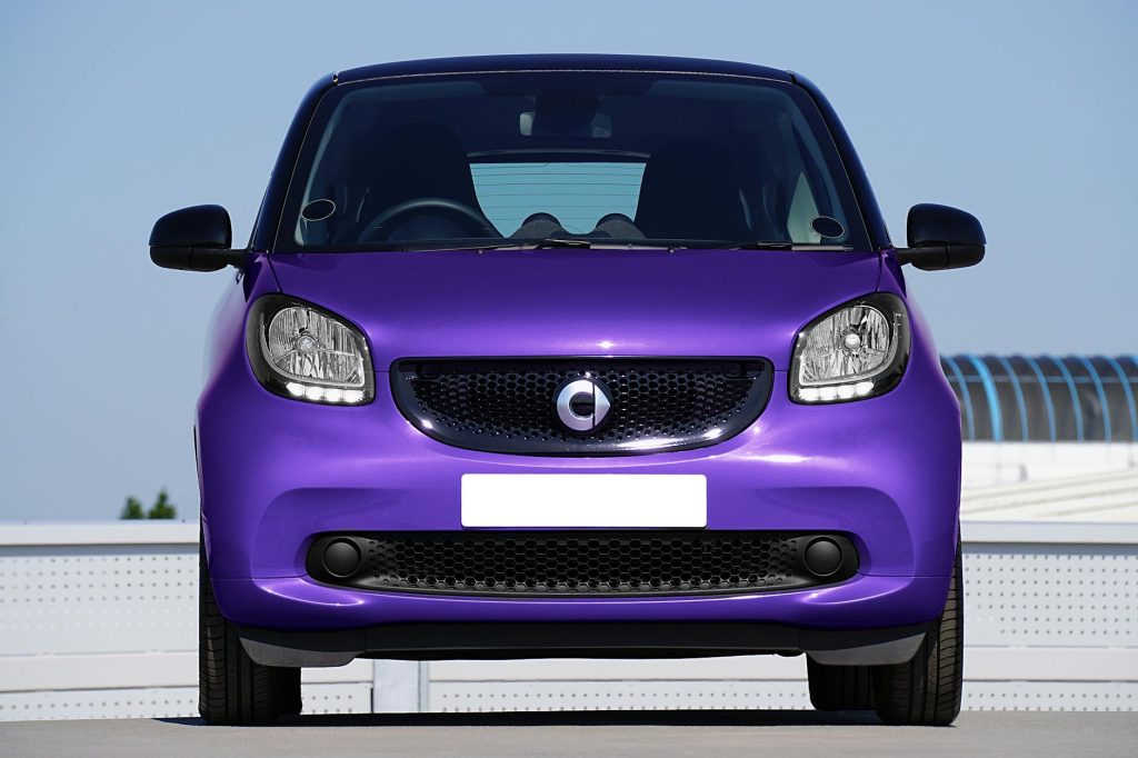 Front view of a vibrant purple Smart car parked outdoors under a clear sky.