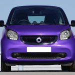 Front view of a vibrant purple Smart car parked outdoors under a clear sky.