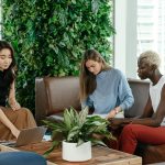 Group of diverse professionals collaborating in a bright, modern office setting with green plants.